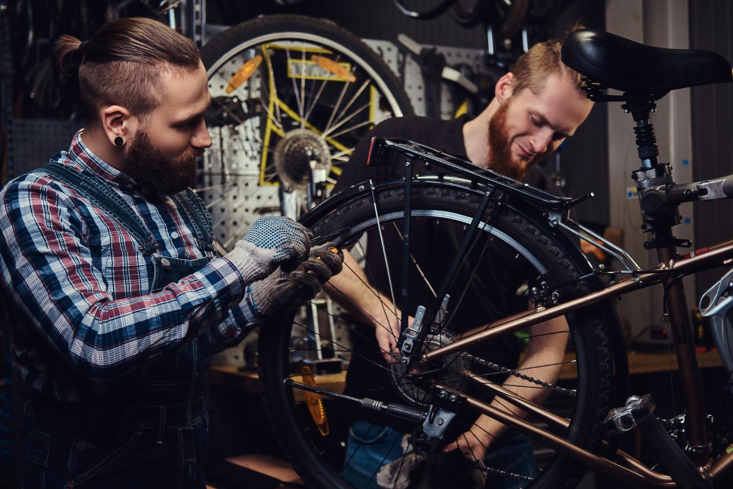 two-handsome-stylish-males-working-with-bicycle-repair-shop-workers-repair-mounts-bike-workshop Two handsome stylish males working with a bicycle in a repair shop. workers repair and mounts bike in a workshop.
